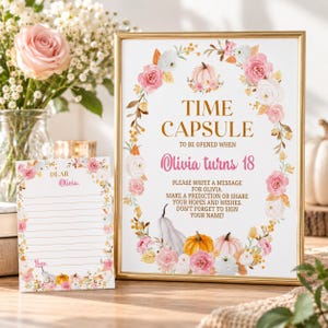 K&ouml;nnte beinhalten: Ein goldgerahmtes Schild und eine passende Karte mit einem Blumenkranz aus rosa und wei&szlig;en Rosen sowie orangefarbenen und wei&szlig;en K&uuml;rbissen. Das Schild tr&auml;gt die Aufschrift: TIME CAPSULE TO BE OPENED WHEN Olivia turns 18. PLEASE WRITE A MESSAGE FOR OLIVIA.