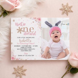 May include: A rectangular birthday invitation card featuring pink floral accents, gold snowflakes, and the text Winter onederland. The card includes details for Isabella's first birthday on October 30th at 5PM, and a photo of a baby in a pink hat.