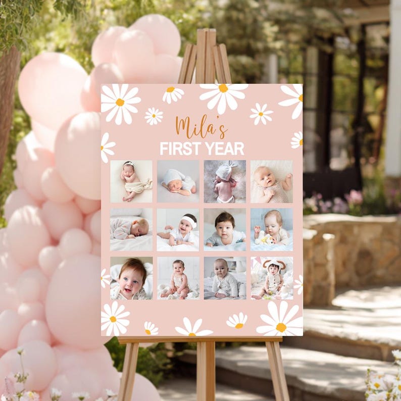 May include: A rectangular sign on a wooden easel featuring a light pink background with white daisy illustrations. The text reads "Mila's FIRST YEAR" above a grid of twelve individual photographs showing a baby at different stages of growth.