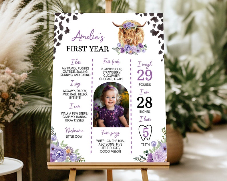 May include: A rectangular milestone sign featuring a cow print border, a highland cow illustration with purple flowers, and text detailing Amelia's first year, including her weight of 29 pounds, height of 28 inches, and 5 teeth, with a central photo.