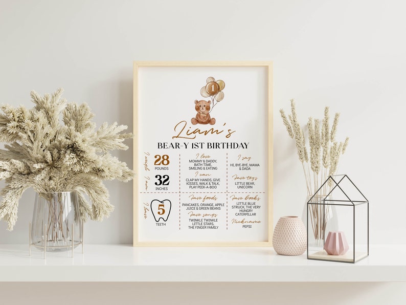Puede incluir: Un cartel de cumplea&ntilde;os enmarcado con un oso de peluche en acuarela que sostiene globos con el n&uacute;mero uno. El texto dice Liam's BEAR-Y 1ST BIRTHDAY, enumerando 28 pounds, 32 inches, 5 dientes y varios favoritos personales en marr&oacute;n y negro.