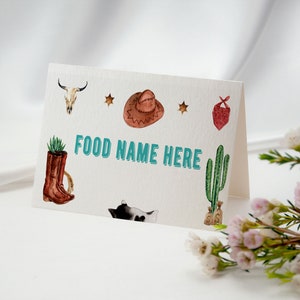 K&ouml;nnte beinhalten: Eine gefaltete wei&szlig;e Karte mit dem Text FOOD NAME HERE in t&uuml;rkisfarbenen Buchstaben. Die Karte ist mit Aquarellillustrationen eines Kuhsch&auml;dels, eines braunen Cowboyhuts, zwei Sternen, einem roten Bandana, einem Stiefel und einem Kaktus verziert.