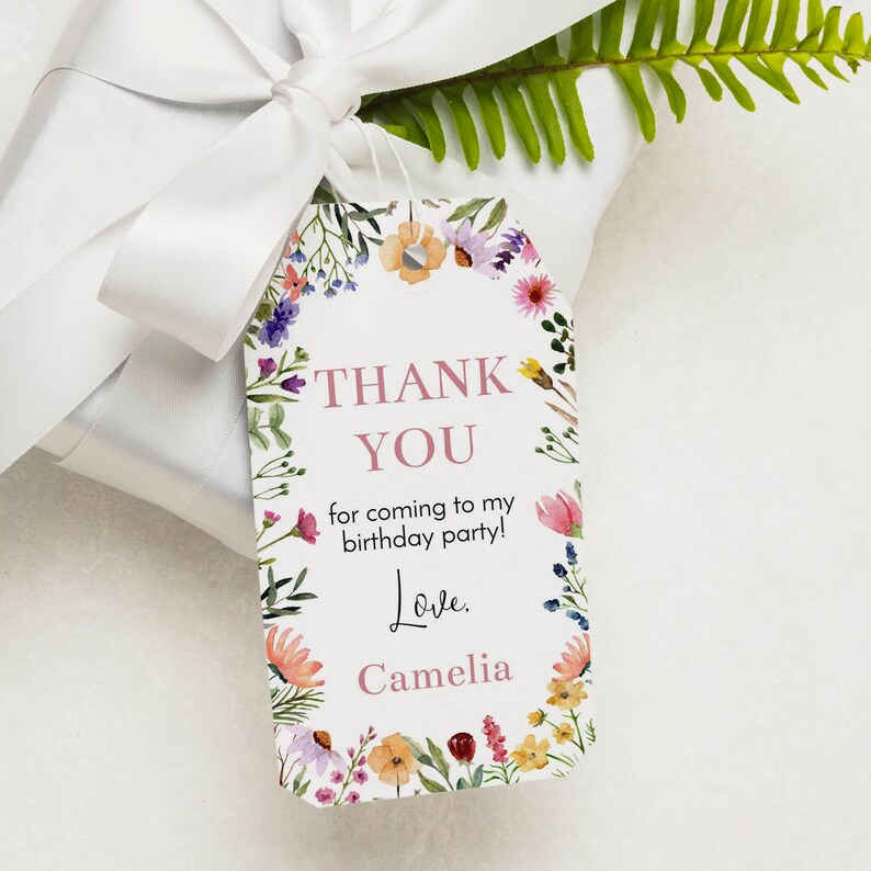 May include: A rectangular white gift tag with rounded top corners, featuring a colorful watercolor floral border. The text reads: THANK YOU for coming to my birthday party! Love. Camelia. The tag is attached to a white gift box with a white ribbon.