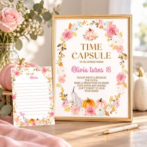 K&ouml;nnte beinhalten: Ein goldgerahmtes Schild und eine passende linierte Karte f&uuml;r eine Zeitkapsel, beide mit Blumenkr&auml;nzen aus rosa Rosen, wei&szlig;en Bl&uuml;ten und K&uuml;rbissen. Das Schild tr&auml;gt die Aufschrift: TIME CAPSULE TO BE OPENED WHEN Olivia turns 18. PLEASE WRITE A MESSAGE.