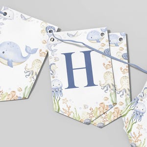 May include: A nautical-themed banner with a light blue ribbon. The banner features watercolor illustrations of whales, jellyfish, octopuses, and other sea creatures. One banner displays the letter "H" in blue.