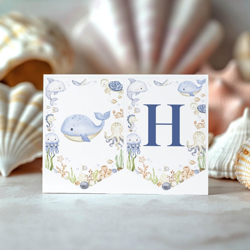 May include: A white banner with a blue letter "H" and watercolor illustrations of marine life, including whales, dolphins, and jellyfish. The banner is decorated with sea creatures and coral, perfect for a nautical-themed event.