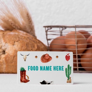 K&ouml;nnte beinhalten: Eine rechteckige wei&szlig;e Karte mit dem Text FOOD NAME HERE in t&uuml;rkisfarbenen Buchstaben. Die Karte ist mit Illustrationen eines Kuhsch&auml;dels, eines braunen Cowboyhuts, eines roten Bandanas, eines braunen Stiefels mit Sukkulente und einer Katze verziert.