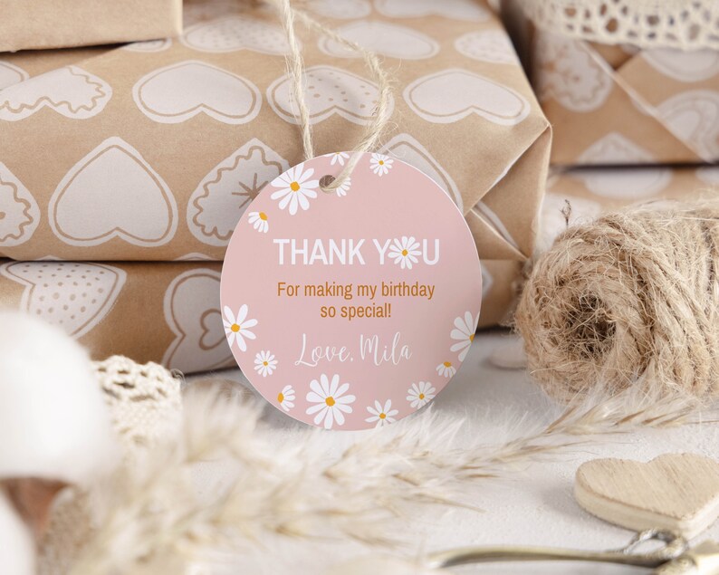 May include: A round, light pink gift tag featuring white daisy illustrations around the border. The text reads: THANK YOU, For making my birthday so special!, Love, Mila. The tag is attached to a piece of twine and has a hole at the top.