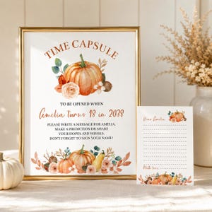 Może przedstawiać: Złota ramka ze znakiem i pasująca karta z akwarelowymi dyniami, kwiatami i eukaliptusem. Znak zawiera napis: TIME CAPSULE TO BE OPENED WHEN Amelia turns 18 in 2038. PLEASE WRITE A MESSAGE FOR AMELIA. MAKE A PREDICTION OR SHARE YOUR HOPES.