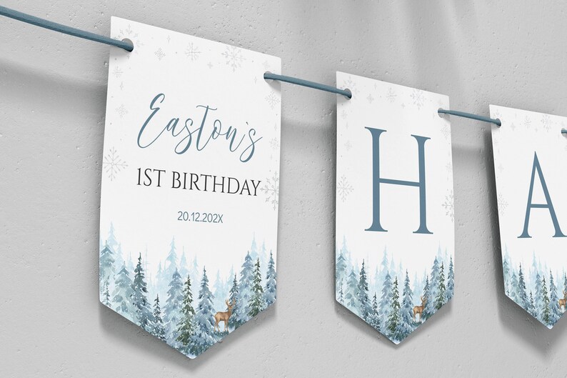 Puede incluir: Una serie de banderines rectangulares blancos colgados de una cuerda azul, con un bosque en acuarela azul, un ciervo, copos de nieve y el texto Easton's 1ST BIRTHDAY 20.12.202X, seguidos de letras individuales que forman un mensaje.