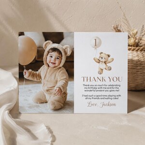 May include: A rectangular thank you card featuring a photo of a child in a tan bear-ear jumpsuit holding a beige balloon. The right side displays a watercolor teddy bear with a balloon labeled 1, the text THANK YOU, and the name Love, Jackson.