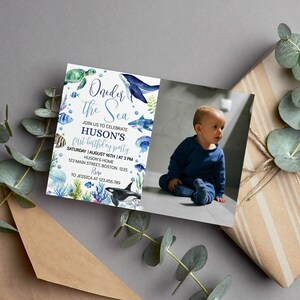 May include: A blue and green invitation card with a watercolor illustration of sea creatures, including a whale, a shark, and a turtle. The text on the card reads "Under the Sea" and "Huson's First Birthday Party". The card also includes a photo of a baby boy.