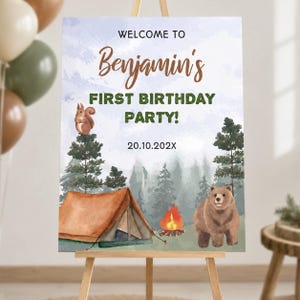 Op de afbeelding: Een rechthoekig welkomstbord voor een eerste verjaardag met een aquarel bossc&egrave;ne, een bruine tent, een kampvuur, een eekhoorn en een beer. De tekst luidt WELCOME TO Benjamin's FIRST BIRTHDAY PARTY! en de datum 20.10.202X.