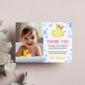 May include: A rectangular thank you card featuring a photograph of a smiling child in a bathtub with a yellow rubber duck. The right side displays a watercolor yellow rubber duck with a pink bow, blue bubbles, and the text Thank You, Sophia.
