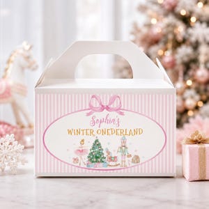 May include: A white gable box featuring a pink striped pattern and a central oval graphic. The graphic displays a pink bow, the text "Sophia's WINTER ONEDERLAND," and illustrations of a ballerina, a Christmas tree, a nutcracker, and a rocking horse.