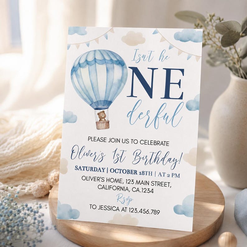 Pu&ograve; includere: Un biglietto d'invito di compleanno rettangolare bianco con una mongolfiera blu ad acquerello e un piccolo orso bruno nel cesto. Il testo recita Isn't he ONEderful, PLEASE JOIN US TO CELEBRATE Oliver's 1st Birthday e i dettagli dell'evento.