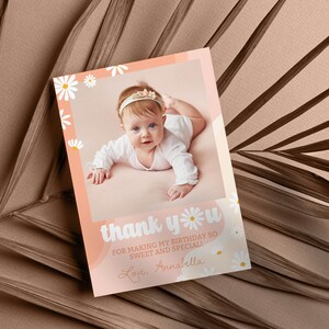 May include: A rectangular birthday thank you card featuring a photograph of a baby wearing a white headband. The card has a peach-colored border decorated with white daisy illustrations and the text: thank you FOR MAKING MY BIRTHDAY SO SWEET AND SPECIAL! Love, Annabella.