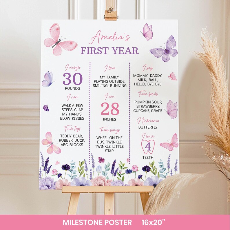 May include: A white milestone poster titled Amelia's First Year, featuring pink and purple butterflies and floral illustrations. The text includes weight in pounds, height in inches, favorite foods, songs, toys, and milestones for a one-year-old.
