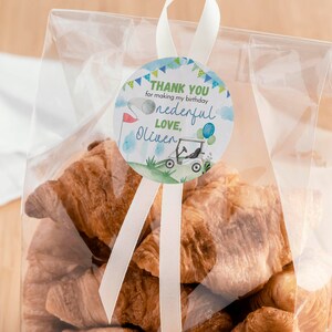 May include: A clear plastic bag filled with golden-brown croissants, sealed with a white ribbon and a round sticker. The sticker features a golf cart, a flag, and the text: THANK YOU for making my birthday onederful LOVE, Oliver.