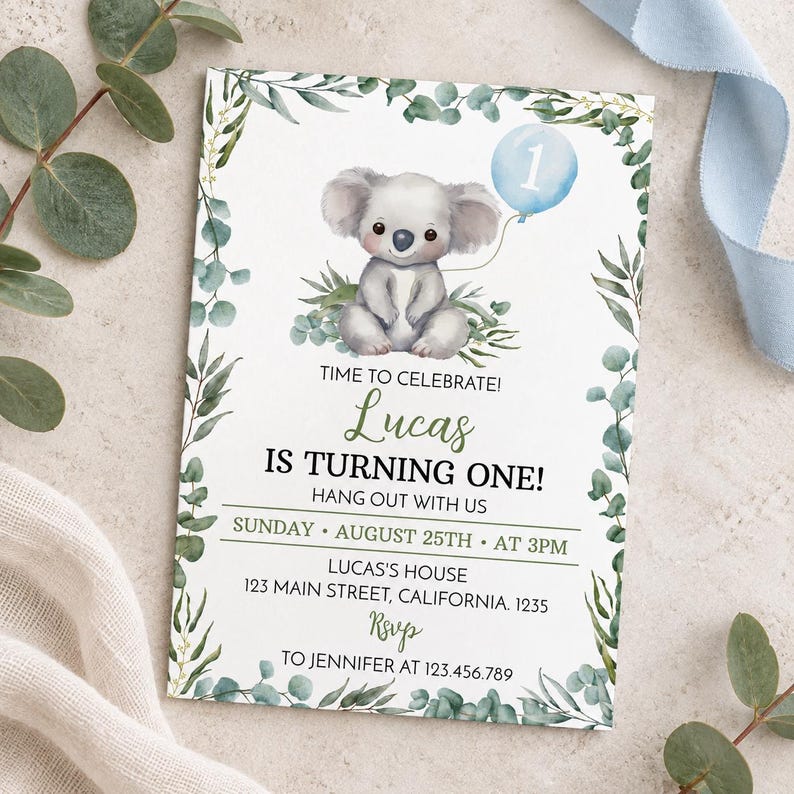 May include: A rectangular birthday invitation card featuring a watercolor illustration of a koala holding a light blue balloon with the number one. The card is framed by green eucalyptus leaves and includes text details for Lucas's first birthday party.