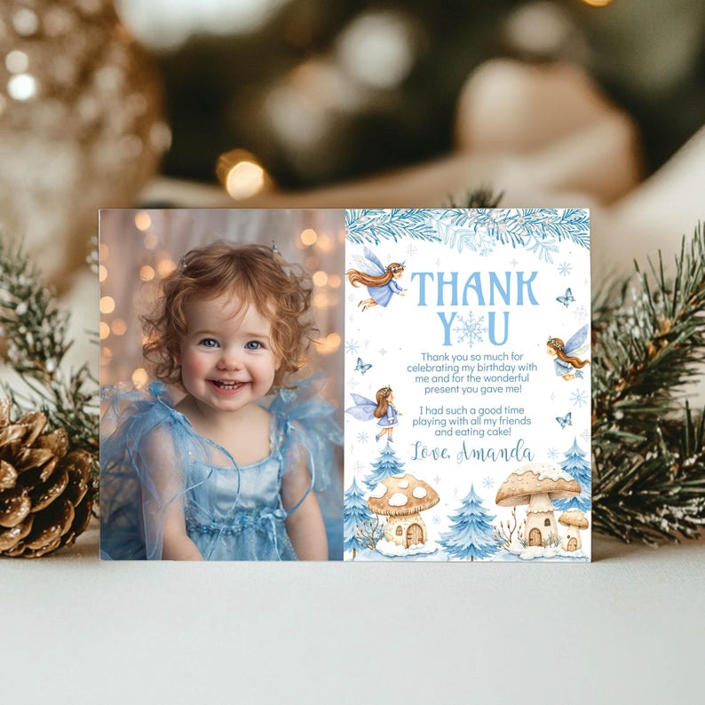 May include: A rectangular thank you card featuring a photograph of a toddler in a blue dress on the left and blue winter-themed illustrations of fairies, mushrooms, and pine trees with the text Thank You and Love, Amanda on the right.