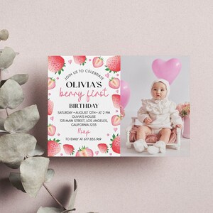 May include: A rectangular birthday invitation card featuring a white background with watercolor strawberries and pink hearts. The text reads: JOIN US TO CELEBRATE OLIVIA'S berry first BIRTHDAY, SATURDAY AUGUST 12TH AT 2 PM, OLIVIA'S HOUSE, 123 MAIN STREET, LOS ANGELES, CALIFORNIA, 1235, RSVP TO EMILY AT 677.855.969. The right side displays a photograph of a baby in a white outfit sitting in a small chair with pink balloons.
