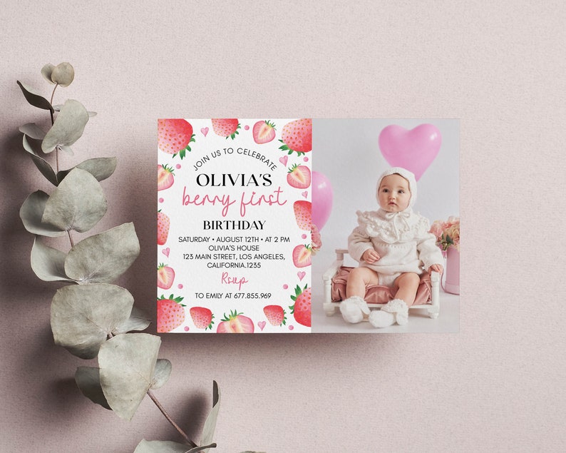 May include: A rectangular birthday invitation card featuring a white background with watercolor strawberries and pink hearts. The text reads: JOIN US TO CELEBRATE OLIVIA'S berry first BIRTHDAY, SATURDAY AUGUST 12TH AT 2 PM, OLIVIA'S HOUSE, 123 MAIN STREET, LOS ANGELES, CALIFORNIA, 1235, RSVP TO EMILY AT 677.855.969. The right side displays a photograph of a baby in a white outfit sitting in a small chair with pink balloons.