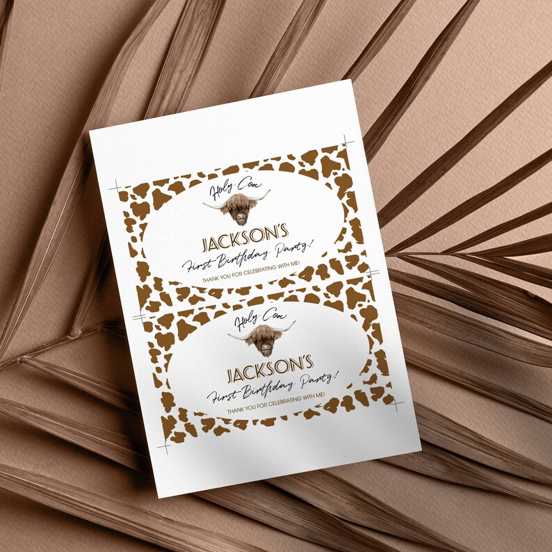 May include: A rectangular sheet featuring two identical oval labels with a brown and white cow print border. Each label displays a Highland cow illustration, the text Holy Cow, JACKSON'S First Birthday Party!, and THANK YOU FOR CELEBRATING WITH ME!