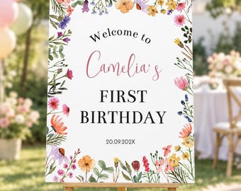 May include: A rectangular welcome sign featuring a watercolor floral border with various colorful wildflowers. The text reads Welcome to Camelia's FIRST BIRTHDAY 20.09.202X. The sign is displayed on a wooden easel stand against a blurred outdoor background.