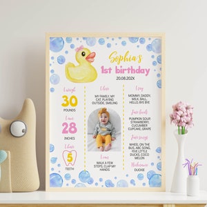 May include: A framed milestone poster for a first birthday featuring a yellow rubber duck, blue watercolor bubbles, and text including Sophia's 1st birthday, 30 pounds, 28 inches, 5 teeth, and personal details alongside a central photograph of a baby.