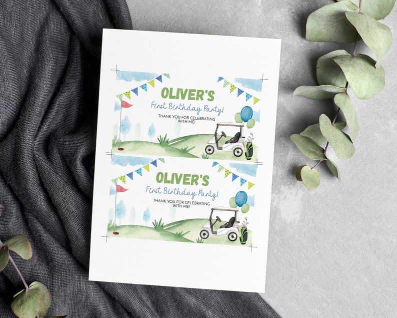 K&ouml;nnte beinhalten: Eine wei&szlig;e rechteckige Karte mit zwei identischen Druckmotiven im Aquarell-Golf-Design. Der Text lautet OLIVER'S First Birthday Party! THANK YOU FOR CELEBRATING WITH ME! Das Design zeigt ein Golfcart, Luftballons und eine Wimpelkette.
