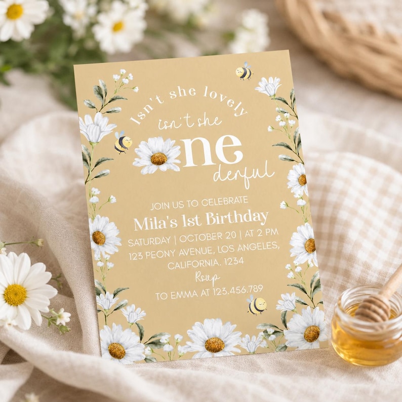May include: A rectangular birthday invitation card on a gold background featuring white daisy illustrations, green leaves, and small bees. The text reads: Isn't she lovely, isn't she one-derful, Join us to celebrate Mila's 1st Birthday, October 20 at 2 PM.