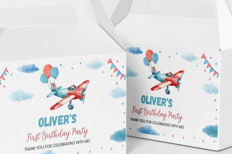 May include: Two white cardboard favor boxes featuring a watercolor illustration of a red and blue airplane with balloons, clouds, and bunting. The text reads: OLIVER'S First Birthday Party THANK YOU FOR CELEBRATING WITH ME! in blue and red ink.