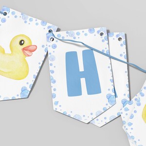 Puede incluir: Una guirnalda decorativa compuesta por banderines blancos unidos por un cordel azul. Cada bander&iacute;n muestra un patito de goma amarillo o una letra H azul grande, rodeados por un patr&oacute;n de acuarela de burbujas azul claro en los bordes.