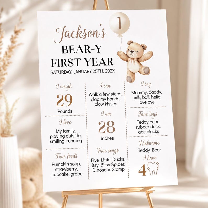 May include: A white milestone birthday sign for Jackson's Bear-y First Year featuring a brown teddy bear illustration, a balloon with the number 1, and text detailing weight in pounds, height in inches, favorite foods, songs, toys, and milestones.