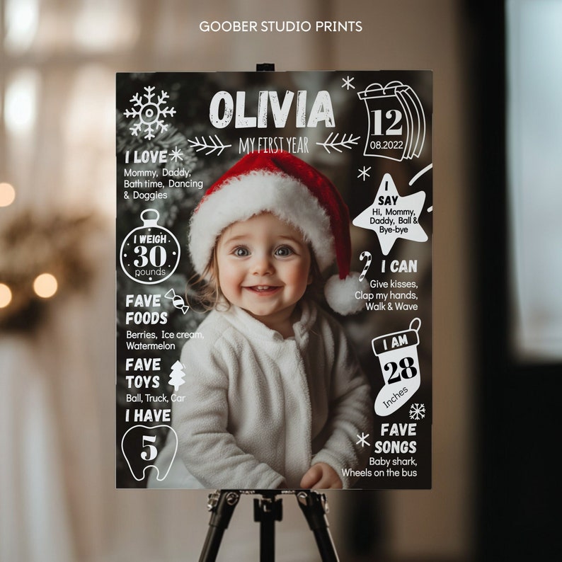 Puede incluir: Un p&oacute;ster de hitos negro titulado Olivia My First Year con la foto de un ni&ntilde;o con gorro de Pap&aacute; Noel. El texto incluye I Love, I Say, I Weigh 13,6 kg, I Can, I Am 71 cm, Fave Foods, Fave Toys, I Have 5 dientes y Fave Songs.