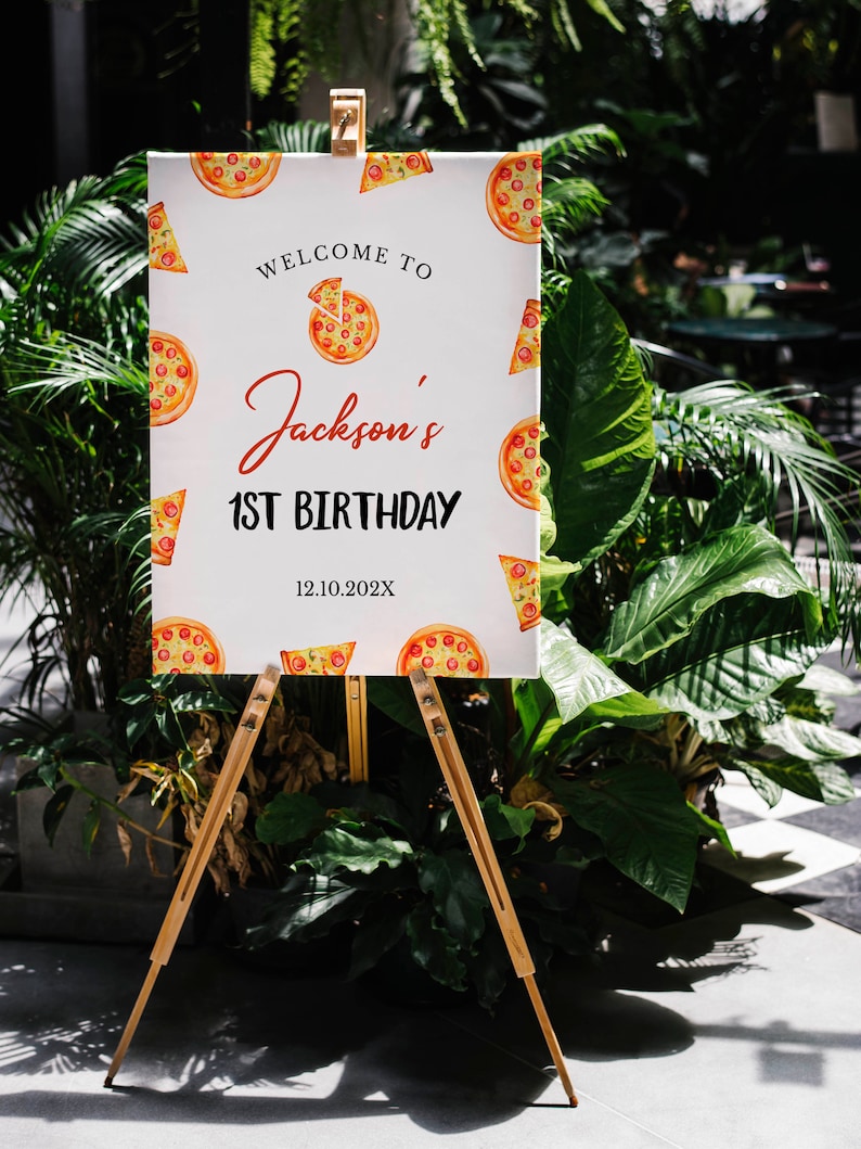 May include: A white sign with a pizza theme welcomes guests to Jackson's 1st Birthday party on 12.10.202X. The sign is on a wooden easel.