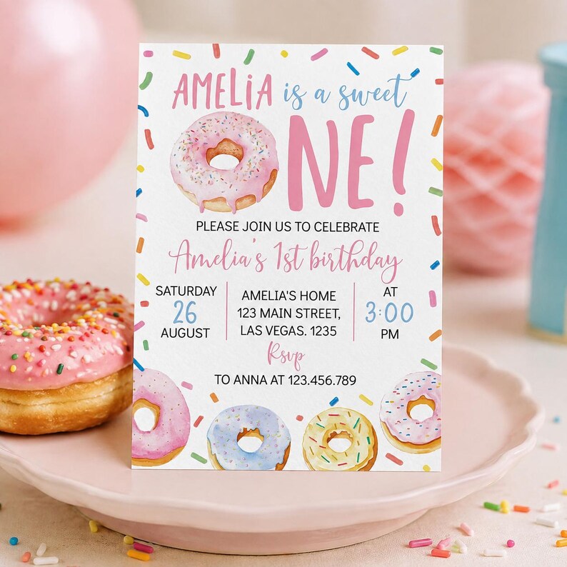 May include: A rectangular birthday invitation card featuring a pink donut illustration, colorful sprinkles, and text that reads: AMELIA is a sweet ONE! PLEASE JOIN US TO CELEBRATE Amelia's 1st birthday SATURDAY 26 AUGUST AT 3:00 PM.