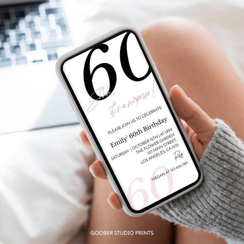 K&ouml;nnte beinhalten: Ein Smartphone zeigt eine digitale Geburtstagseinladung mit dem gro&szlig;en schwarzen Text 60, gefolgt von dem rosa Schreibschrifttext Shhh... it's a surprise! und Details f&uuml;r Emilys 60. Geburtstag am 12. Oktober um 17 Uhr im The Flower Garden.