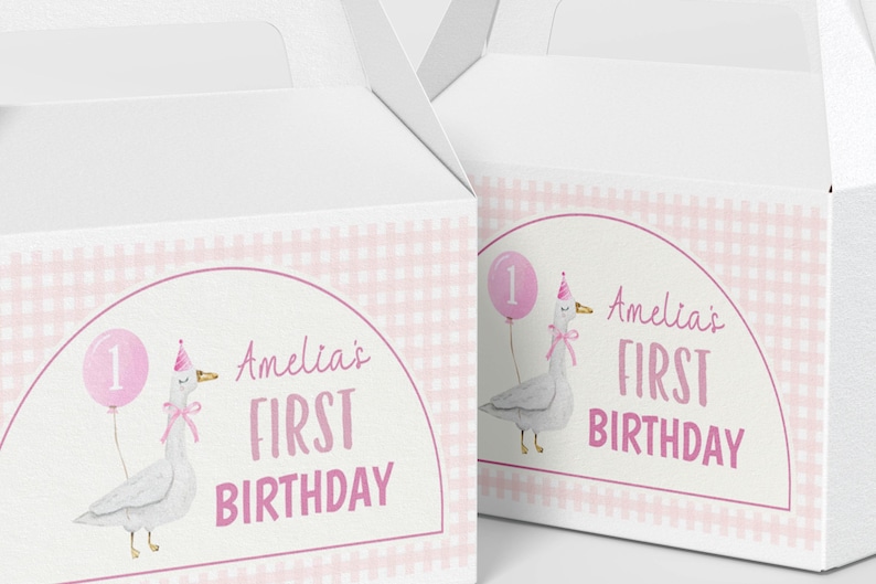 May include: Two white cardboard gable boxes featuring a pink gingham pattern and a central arch graphic. The design includes a watercolor illustration of a goose wearing a party hat, holding a pink balloon with the number one, and the text Amelia's FIRST BIRTHDAY.