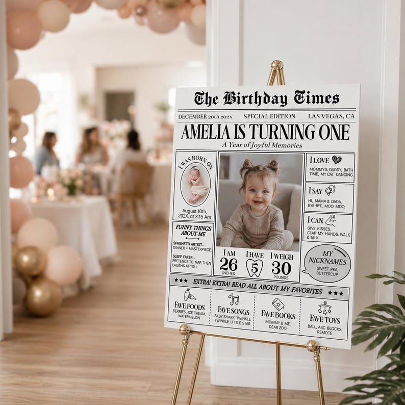 May include: A white rectangular birthday milestone sign titled The Birthday Times featuring a central photograph of a baby, text detailing birth date, height of 66 cm, weight of 13.6 kg, favourite foods, songs, books, and toys in black ink.