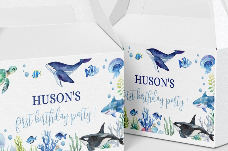 May include: Two white cardboard favor boxes featuring watercolor illustrations of sea creatures including a whale, shark, orca, turtle, jellyfish, and fish. The text HUSON'S first birthday party! is printed in blue on the front of each box.