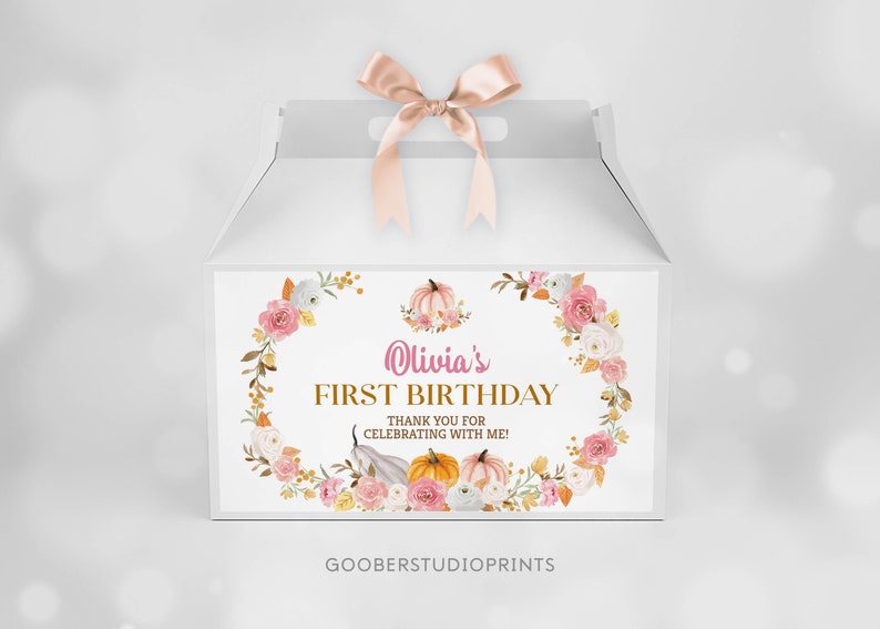 May include: A white gable box with a satin ribbon bow on top. The front features a floral wreath design with pumpkins and the text: Olivia's FIRST BIRTHDAY THANK YOU FOR CELEBRATING WITH ME! The bottom includes the text GOOBERSTUDIOPRINTS.