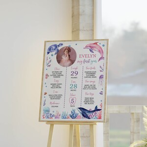 May include: A rectangular milestone poster featuring a circular photo of a child, watercolour sea creatures, and text detailing personal facts including 29 pounds, 28 inches, and 5 teeth. The design includes the name Evelyn and my first year.