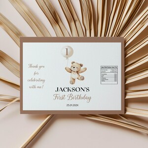May include: A brown thank you card with a teddy bear holding a balloon that says "1". The card says "Thank you for celebrating with me! JACKSON'S First Birthday 25.01.202X" and has a nutrition facts label.