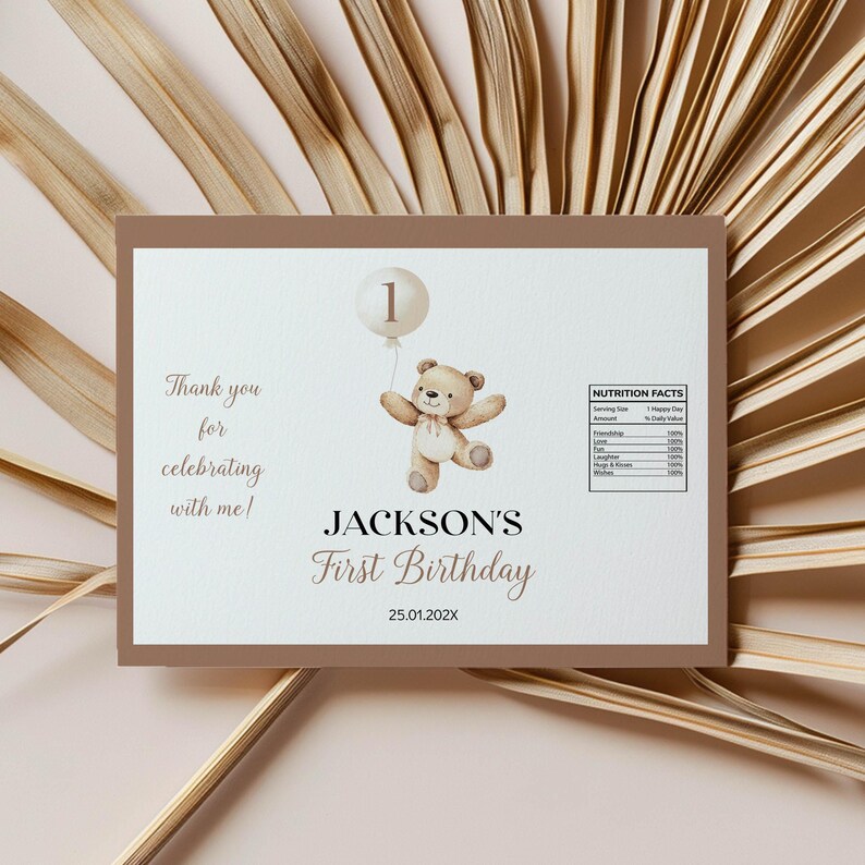 May include: A brown thank you card with a teddy bear holding a balloon that says "1". The card says "Thank you for celebrating with me! JACKSON'S First Birthday 25.01.202X" and has a nutrition facts label.