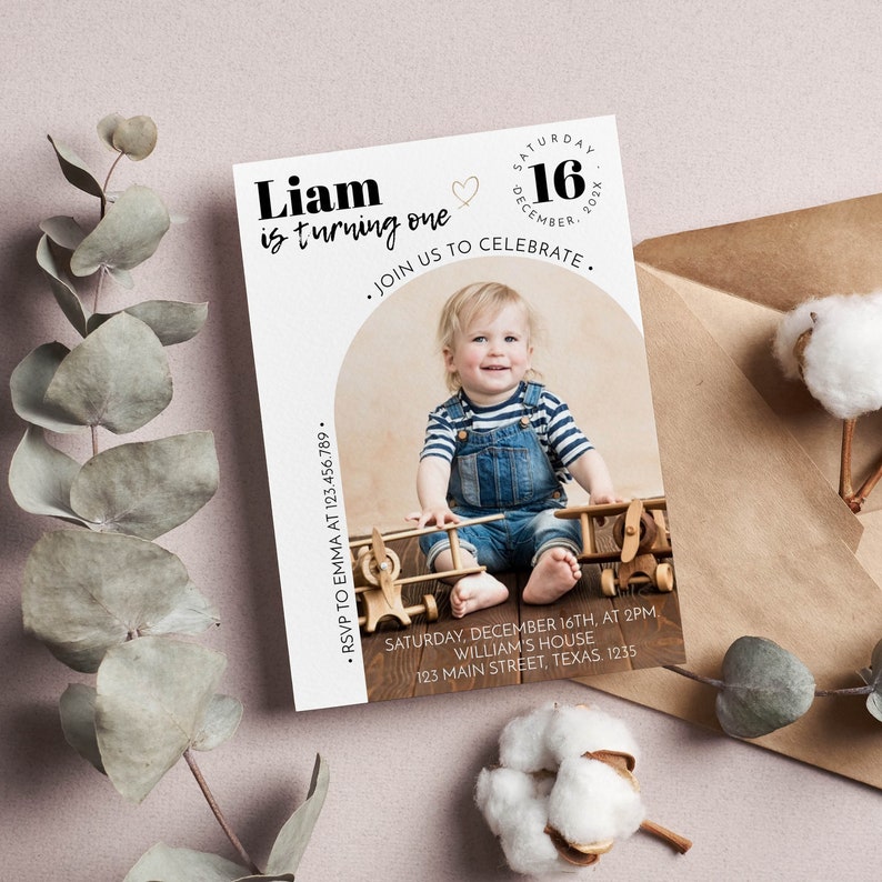 May include: A rectangular birthday invitation card featuring a photo of a child in denim overalls and a striped shirt with wooden toy airplanes. The text reads Liam is turning one, Saturday 16 December 202X, Join us to celebrate, RSVP to Emma at 123.456.789, Saturday, December 16th, at 2pm, William's House, 123 Main Street, Texas. 1235.