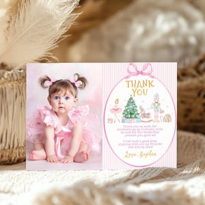 May include: A rectangular thank you card featuring a photograph of a toddler in a pink ruffled dress on the left and a pink striped background with a nutcracker, ballerina, and Christmas tree illustration on the right with the text Thank You.