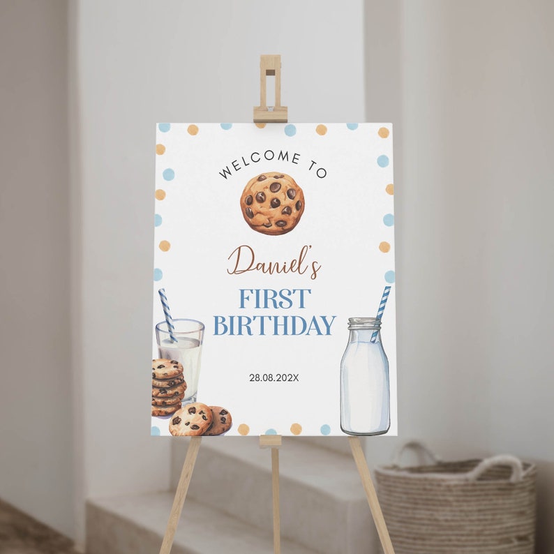 May include: Welcome to Daniel's First Birthday party sign with a blue and orange polka dot background. The sign features a chocolate chip cookie, a glass of milk with a straw, and a bottle of milk. The date 28.08.202X is printed on the sign.