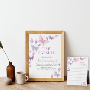 May include: A framed print with the words "TIME CAPSULE" and "Amelia turns 18" with butterfly illustrations. A matching card with "DEAR Amelia" is also present. The frame is made of wood.